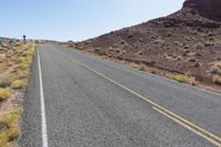 a person riding their bike down a deserted mountain road near a rock formation behind him