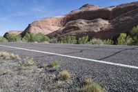 a highway runs through the middle of an arid terrain with sparse vegetation on both sides and large, jagged hills near the top of the road