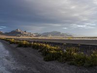 a empty highway with mountains in the background on the horizon at dusk with a sky filled with clouds