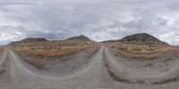 an image of some dirt road and hills in the background with some clouds in the sky