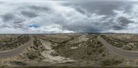 some clouds are over the dirt road and mountains with two curves in it and the sky has a blue cloudy