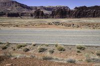 an empty desert area with mountains, road, and grass covered hillsides in the distance