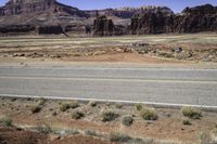 an empty desert area with mountains, road, and grass covered hillsides in the distance