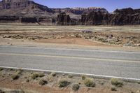 an empty desert area with mountains, road, and grass covered hillsides in the distance