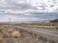 an open field with a dirt road and power lines on both sides of it and some mountains in the distance