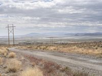 an open field with a dirt road and power lines on both sides of it and some mountains in the distance