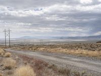 an open field with a dirt road and power lines on both sides of it and some mountains in the distance