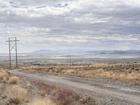 an open field with a dirt road and power lines on both sides of it and some mountains in the distance