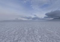 an empty expanse with a mountain in the distance covered in snow and sand, under cloudy skies