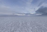 an empty expanse with a mountain in the distance covered in snow and sand, under cloudy skies