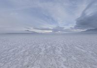 an empty expanse with a mountain in the distance covered in snow and sand, under cloudy skies