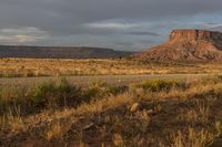 horse grazing in open plain next to tall mountain in distance with dark clouds overhead on a gloom, partly cloudy day