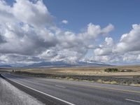 a large highway leads into the mountains with snow capped peaks in the background on a clear day