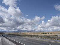 a large highway leads into the mountains with snow capped peaks in the background on a clear day