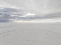 the sky has clouds above a large plain of sand in a desert area, with tracks of vehicles on it