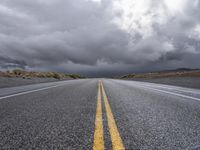 a straight highway going through the desert with storm clouds overhead the road is empty and not being used for vehicles