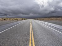 a straight highway going through the desert with storm clouds overhead the road is empty and not being used for vehicles