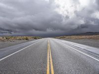 a straight highway going through the desert with storm clouds overhead the road is empty and not being used for vehicles