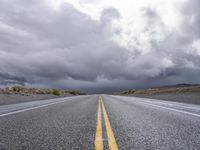 a straight highway going through the desert with storm clouds overhead the road is empty and not being used for vehicles