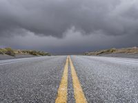 a straight highway going through the desert with storm clouds overhead the road is empty and not being used for vehicles