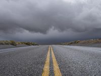 a straight highway going through the desert with storm clouds overhead the road is empty and not being used for vehicles