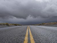 a straight highway going through the desert with storm clouds overhead the road is empty and not being used for vehicles