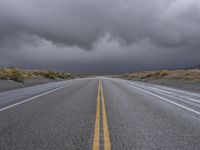 a straight highway going through the desert with storm clouds overhead the road is empty and not being used for vehicles