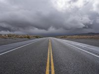 a straight highway going through the desert with storm clouds overhead the road is empty and not being used for vehicles