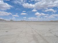 a wide shot of an empty dirt field in the middle of a desert area with mountains and blue sky in the background