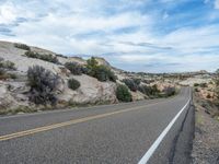 the highway leading towards the rocky cliff side, with yellow lines on it, is next to a white line in the road