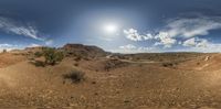 the 360 view of a dirt road near a rocky hill in front of a sunlit sky