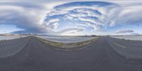 a view of an empty road with large clouds overhead and a highway stretching out across it