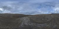 view of a large open area with a hill in the background, clouds are floating over