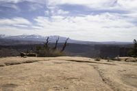 a small rock formation with view of some mountain ranges behind it in desert landscape with trees and shrubs