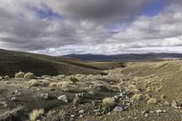 dirt hills in an arid field with rocky ground and a blue sky overhead on a cloudy day