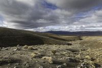 dirt hills in an arid field with rocky ground and a blue sky overhead on a cloudy day