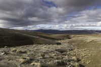 dirt hills in an arid field with rocky ground and a blue sky overhead on a cloudy day