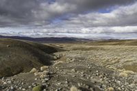 dirt hills in an arid field with rocky ground and a blue sky overhead on a cloudy day