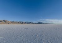 tracks in the sand leading into nowhere with mountains in the background with blue sky in a photograph