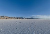 tracks in the sand leading into nowhere with mountains in the background with blue sky in a photograph