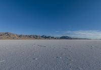 tracks in the sand leading into nowhere with mountains in the background with blue sky in a photograph