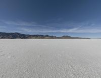 an open plain with mountains and clouds in the background and some tracks in the water