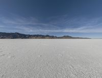 an open plain with mountains and clouds in the background and some tracks in the water