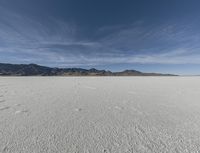 an open plain with mountains and clouds in the background and some tracks in the water