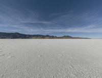 an open plain with mountains and clouds in the background and some tracks in the water