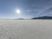 an empty desert plain with mountains in the background and a bright sky and sun in the middle