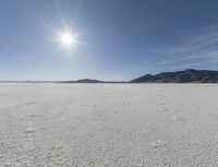 an empty desert plain with mountains in the background and a bright sky and sun in the middle