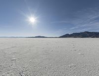 an empty desert plain with mountains in the background and a bright sky and sun in the middle