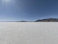 an empty desert plain with mountains in the background and a bright sky and sun in the middle