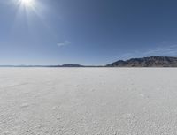 an empty desert plain with mountains in the background and a bright sky and sun in the middle